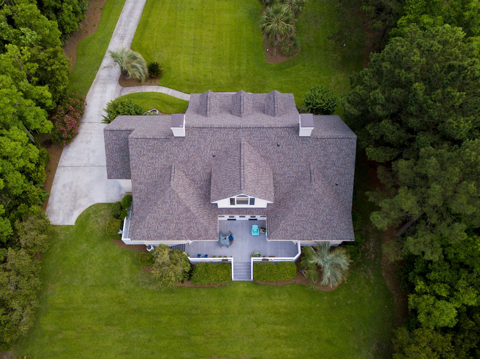 Aerial view of a gray architectural shingle roof on a large house surrounded by green grass and trees