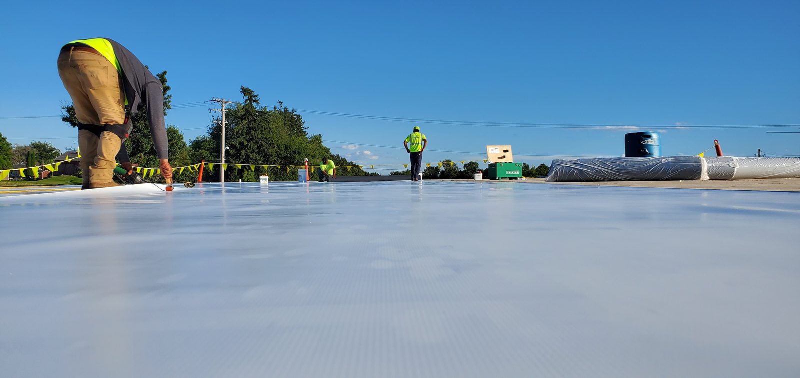 Roofing crew working on a white membrane roof under a clear blue sky