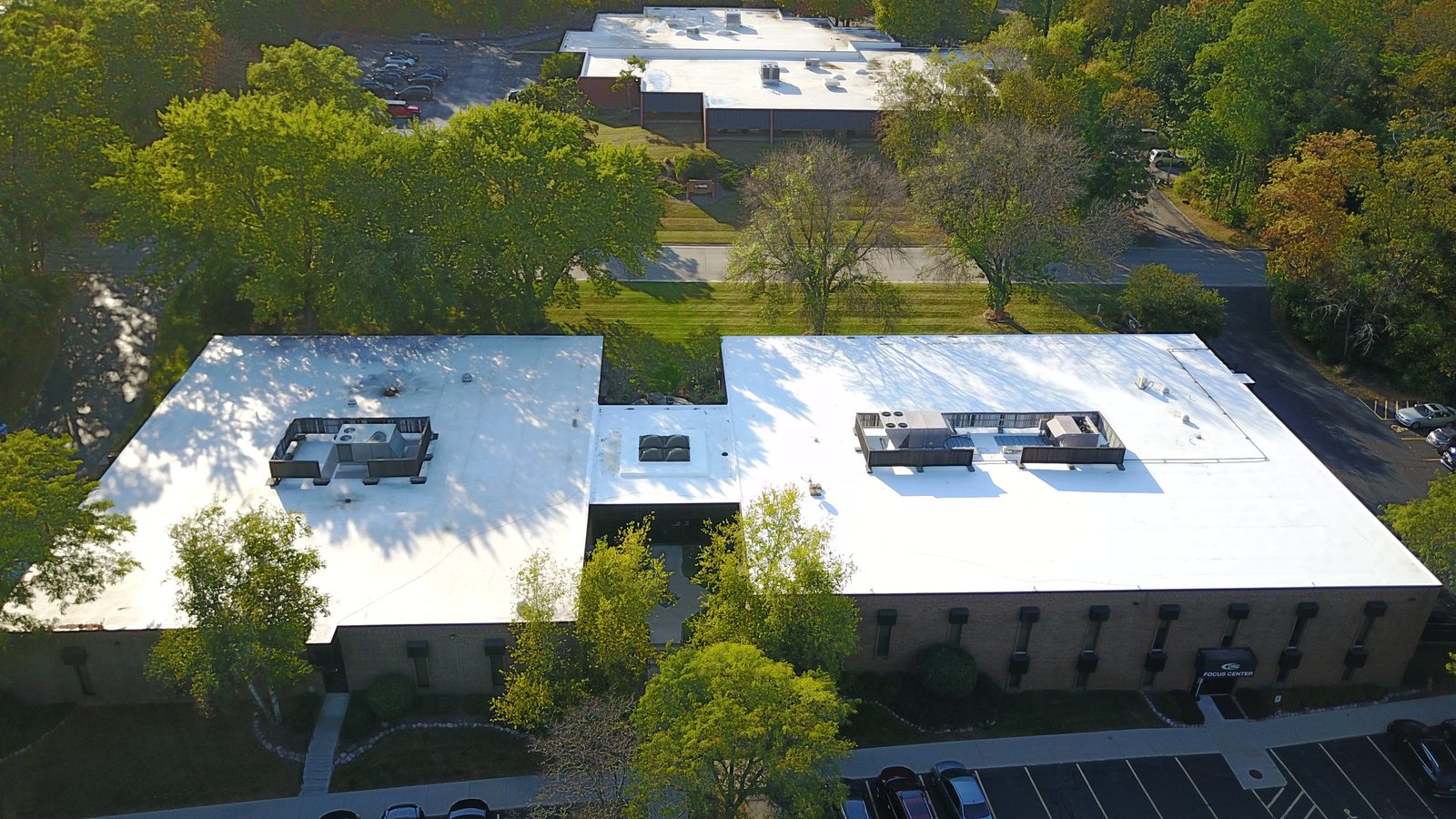Aerial view of a two-wing commercial building with a large white flat roof and rooftop HVAC units